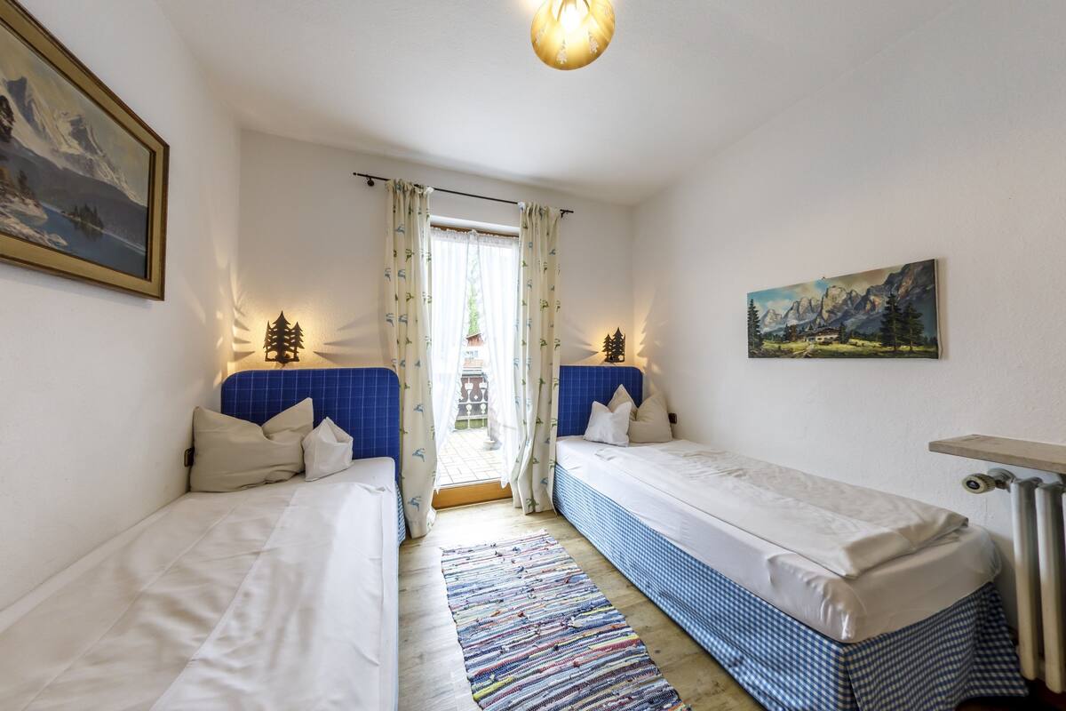Een kamer met twee bedden, een raam met gordijnen, een radiator en een schilderij aan de muur.