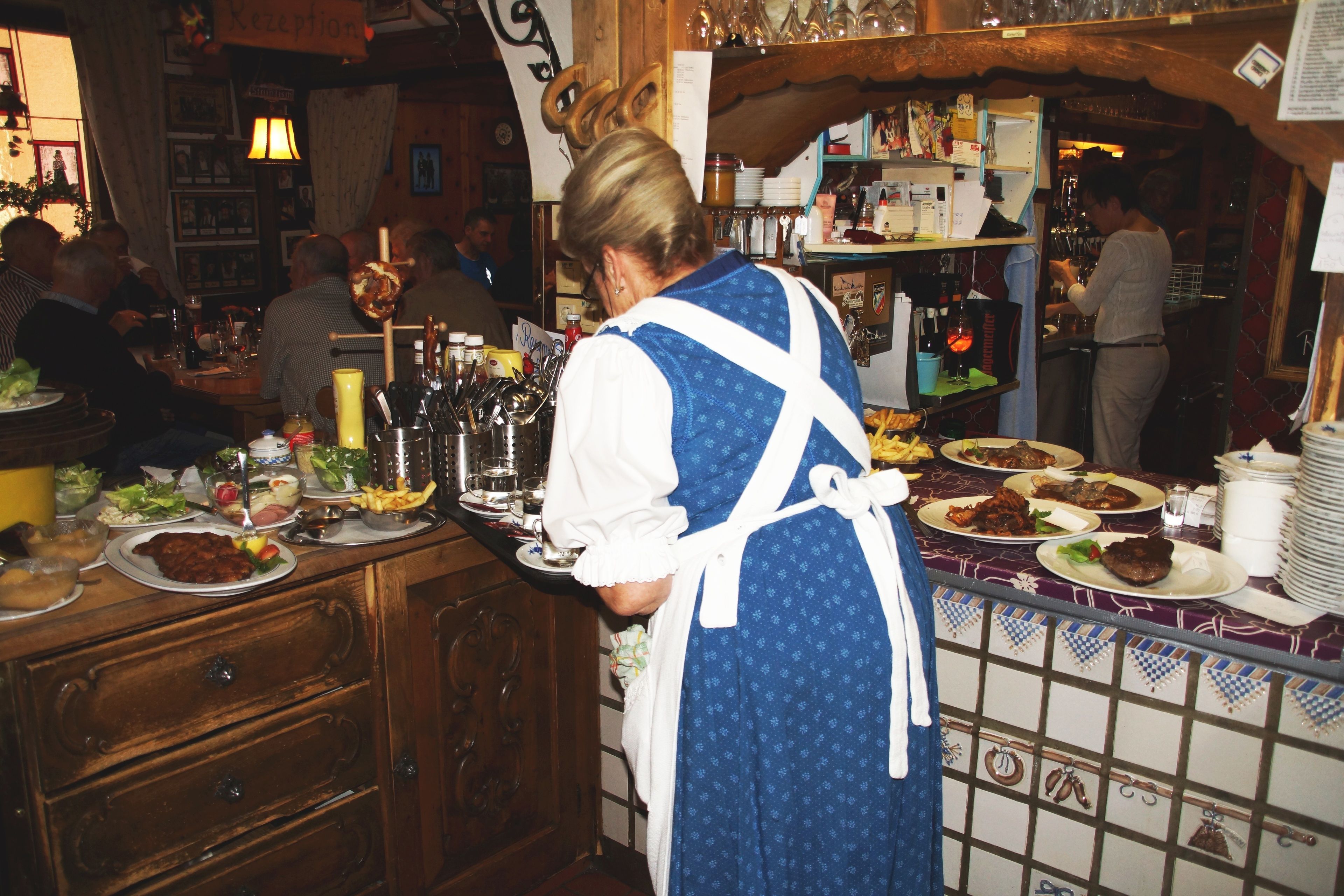 A person serving food in a restaurant with wooden furniture and a tiled backsplash.