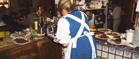 A person serving food in a restaurant with wooden furniture and a tiled backsplash.