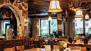 Interior de restaurante com mesas de madeira, luminárias pendentes e diversos pratos e utensílios sobre as mesas.