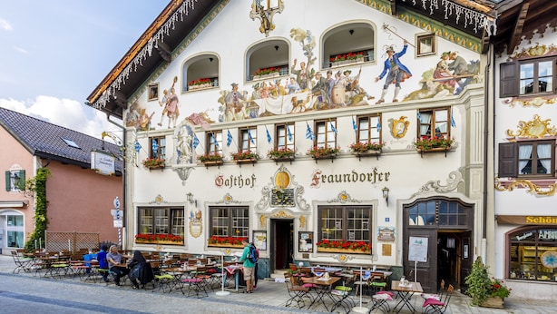 Um edifício bávaro tradicional com um mural retratando cenas históricas, uma placa com o nome 