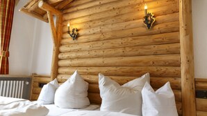 Interior de uma cabana de madeira com uma cama, almofadas brancas e duas luminárias fixadas na parede.