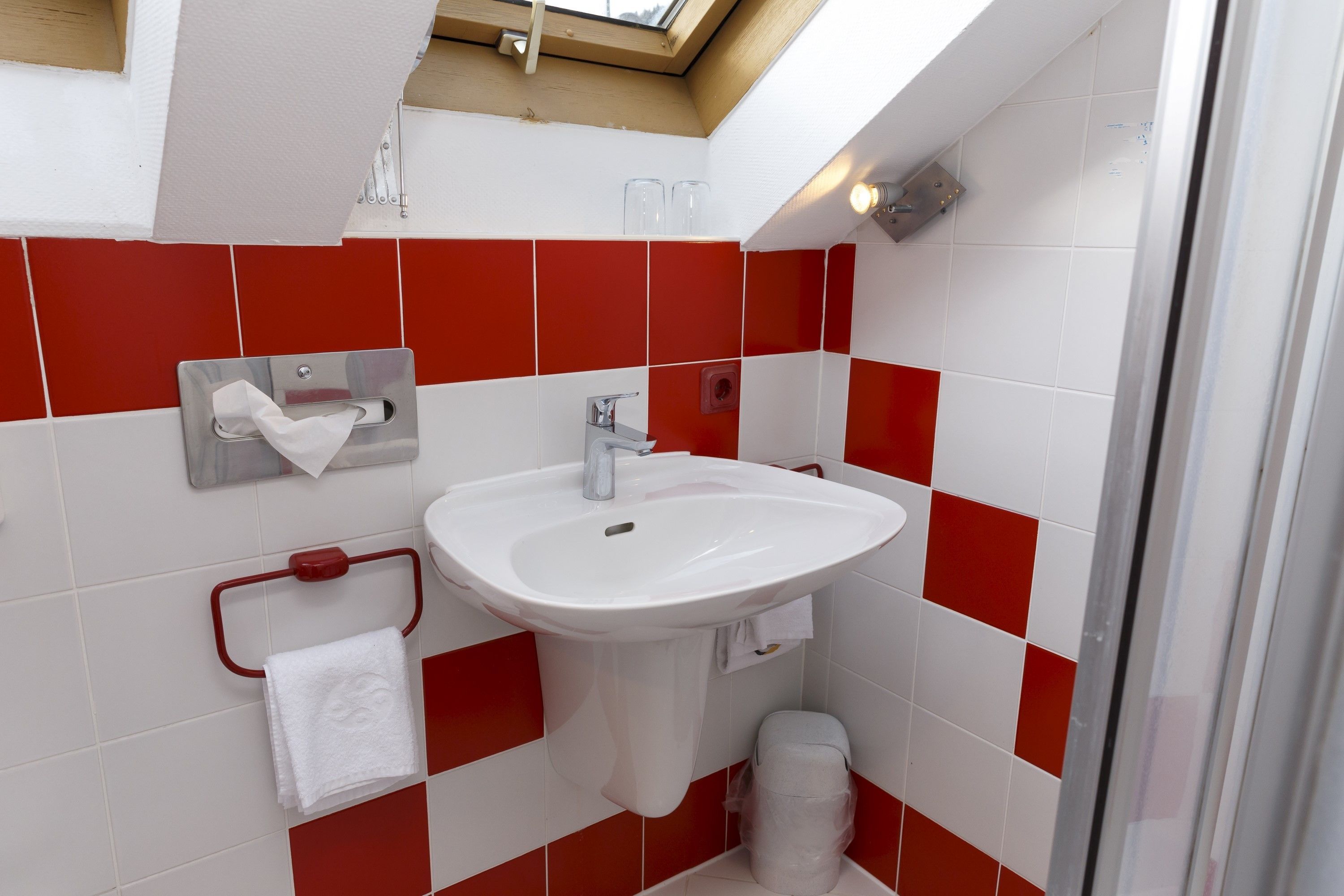 A bathroom with a white sink, red and white tiles, a towel rack, and a trash bin.