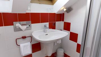 A bathroom with a white sink, red and white tiles, a towel rack, and a trash bin.