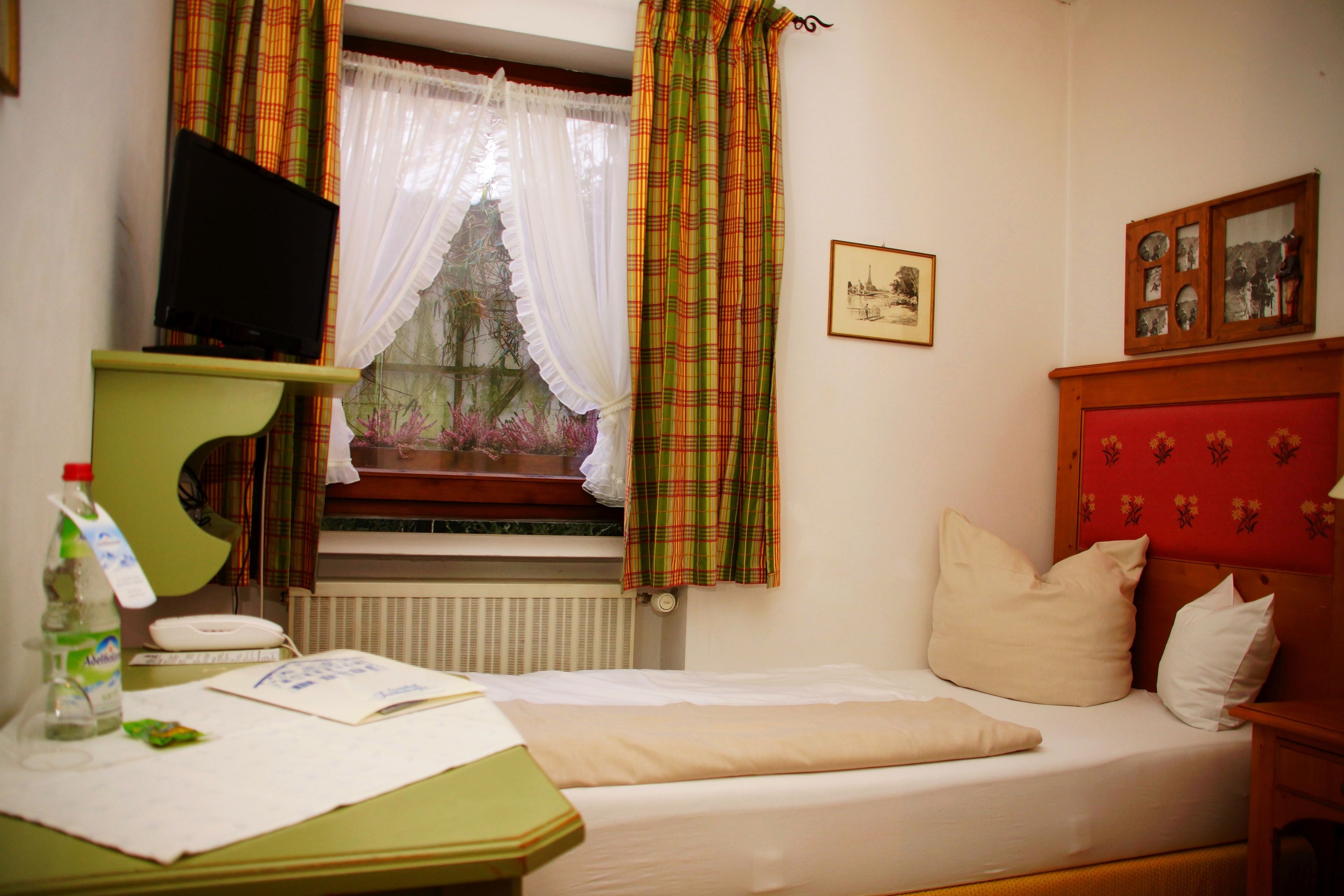 A bedroom with a bed, a desk with a computer, a window with curtains, and a radiator.