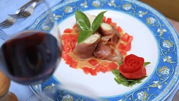 Un plato de comida con una decoración de rosa, una copa de vino tinto y un mantel de estampado azul.
