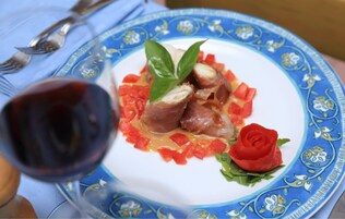 Un plato de comida con una decoración de rosa, una copa de vino tinto y un mantel de estampado azul.