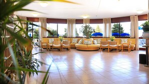 A hotel lobby with a curved sofa, chairs, and potted plants. - Hotel Soleado (Alghero)