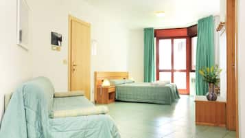 Una habitación con dos camas, una puerta de madera, una mesita de noche, una lámpara, una planta y una ventana con cortinas.
