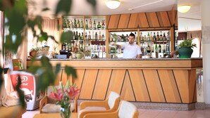 A bar area with a wooden counter, shelves with various bottles, and a few chairs. - Hotel Soleado (Alghero)