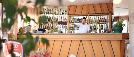 A bar area with a wooden counter, shelves with various bottles, and a few chairs.