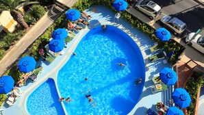 A large outdoor swimming pool with multiple lanes, surrounded by lounge chairs and umbrellas. - Hotel Soleado (Alghero)