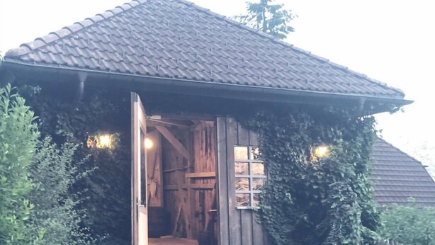 Un bâtiment rustique en bois, doté d’un toit en tuiles, d’une porte ouverte donnant sur l’intérieur et d’un petit porche.