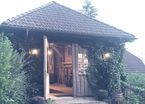 Ein rustikales Holzgebäude mit Ziegeldach, einer offenen Tür und einem kleinen Vorbereich.