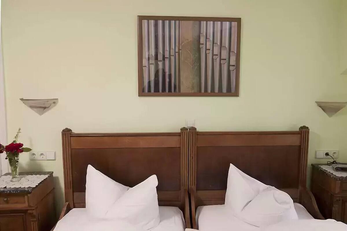 Een tweepersoonsbed met een houten hoofdeinde, twee nachtkastjes en een vaas met rode bloemen aan de linkerkant.