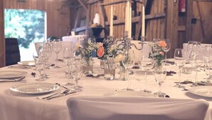 Une table dressée pour un événement formel, dans une pièce rustique en bois, agrémentée de chandeliers et de compositions florales.