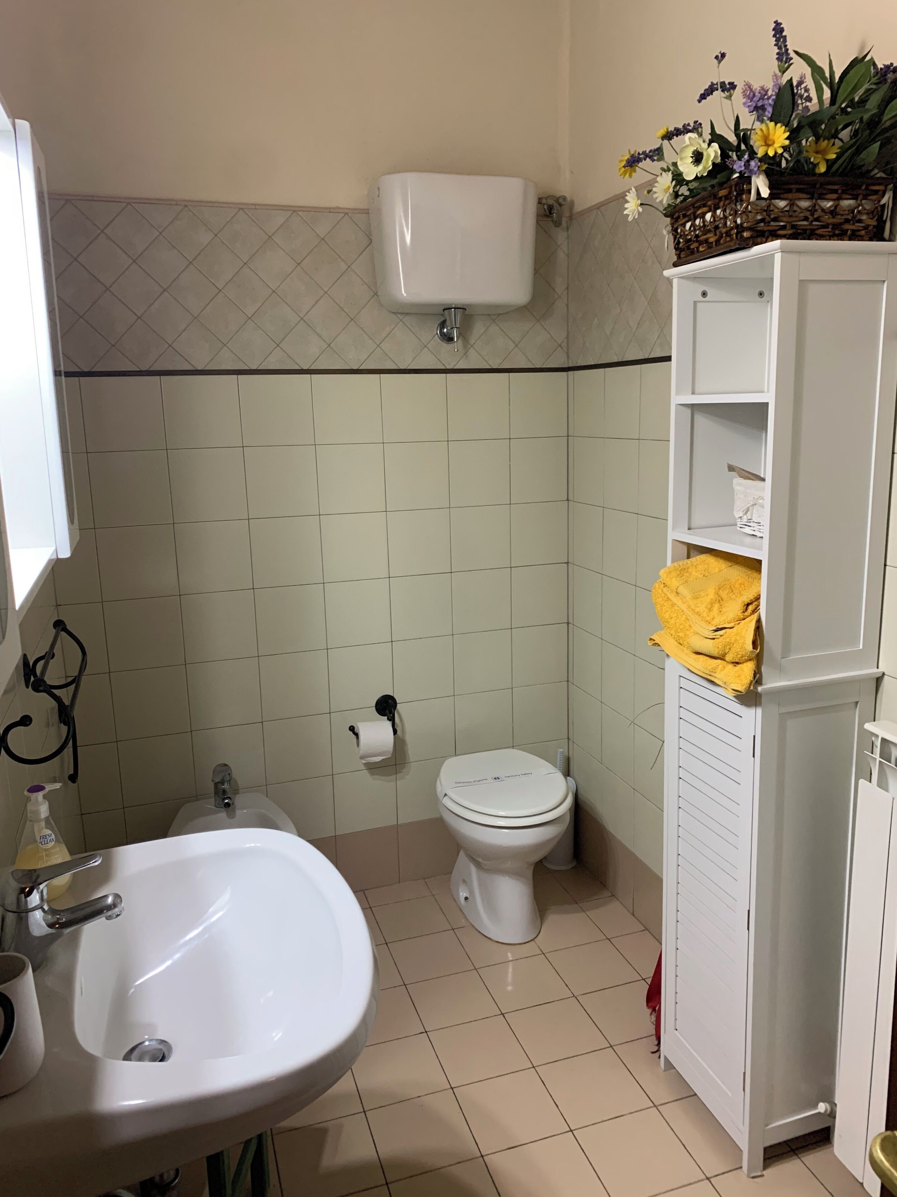 A bathroom with a sink, toilet, and a basket of flowers on a shelf.