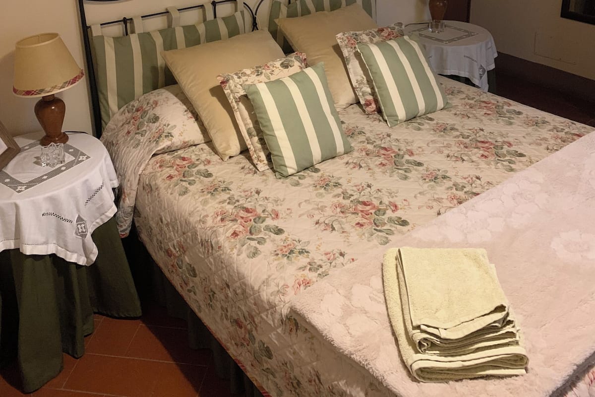 A neatly made bed with floral bedding, a metal headboard, and two bedside tables with lamps.