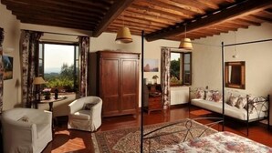 A cozy room with a wooden ceiling, a sofa, a chair, a cabinet, and a window with curtains. - La Canonica di San Michele (Monteriggioni)