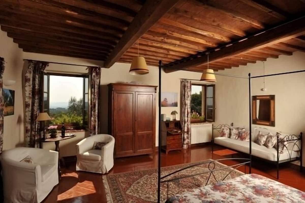 A cozy room with a wooden ceiling, a sofa, a chair, a cabinet, and a window with curtains.