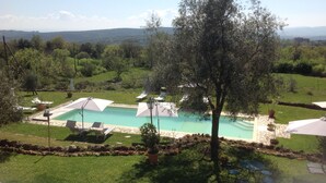 A pool area with lounge chairs and umbrellas, surrounded by a stone deck and lush greenery. - La Canonica di San Michele (Monteriggioni)