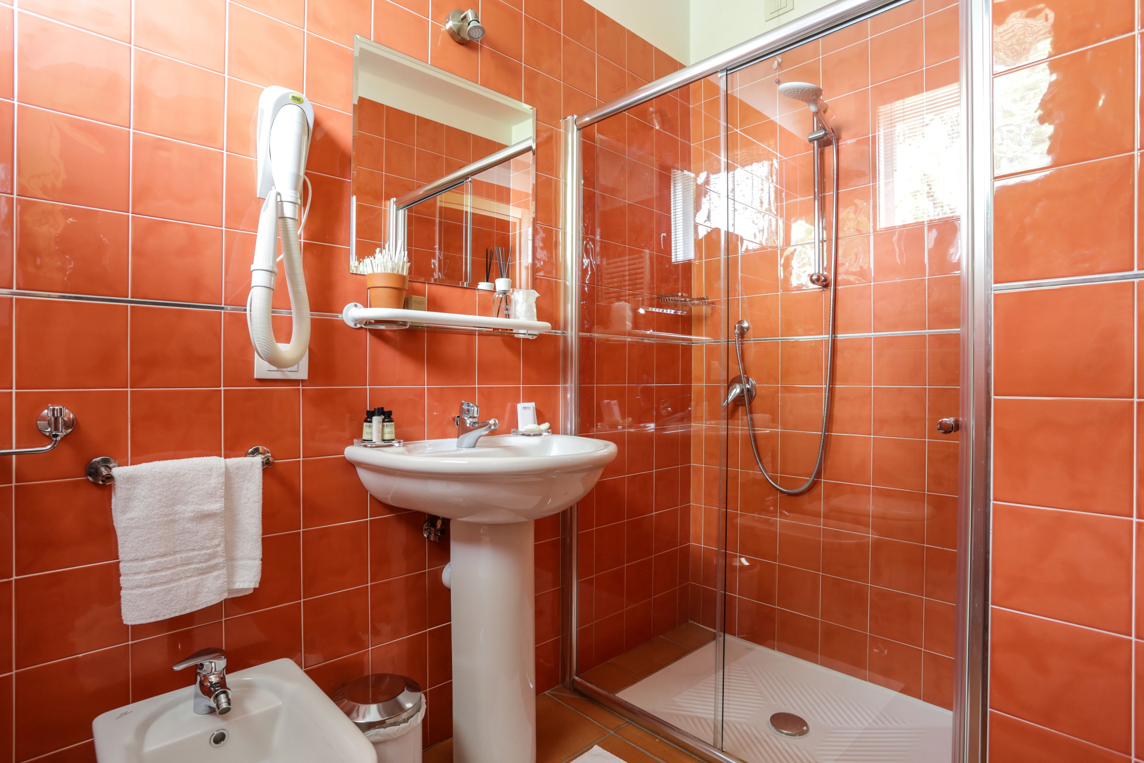 A bathroom with a glass-enclosed shower, a pedestal sink, and a hand dryer.