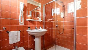 A bathroom with a glass-enclosed shower, a pedestal sink, and a hand dryer.