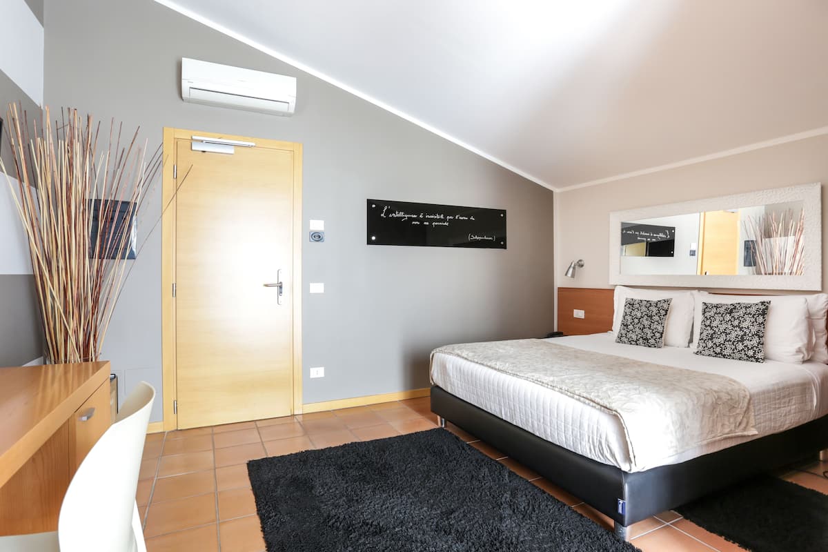 Ein Schlafzimmer mit einem Bett, einem Schreibtisch, einem Stuhl, einem schwarzen Teppich, einer Holztür und einer Wand-Klimaanlage.
