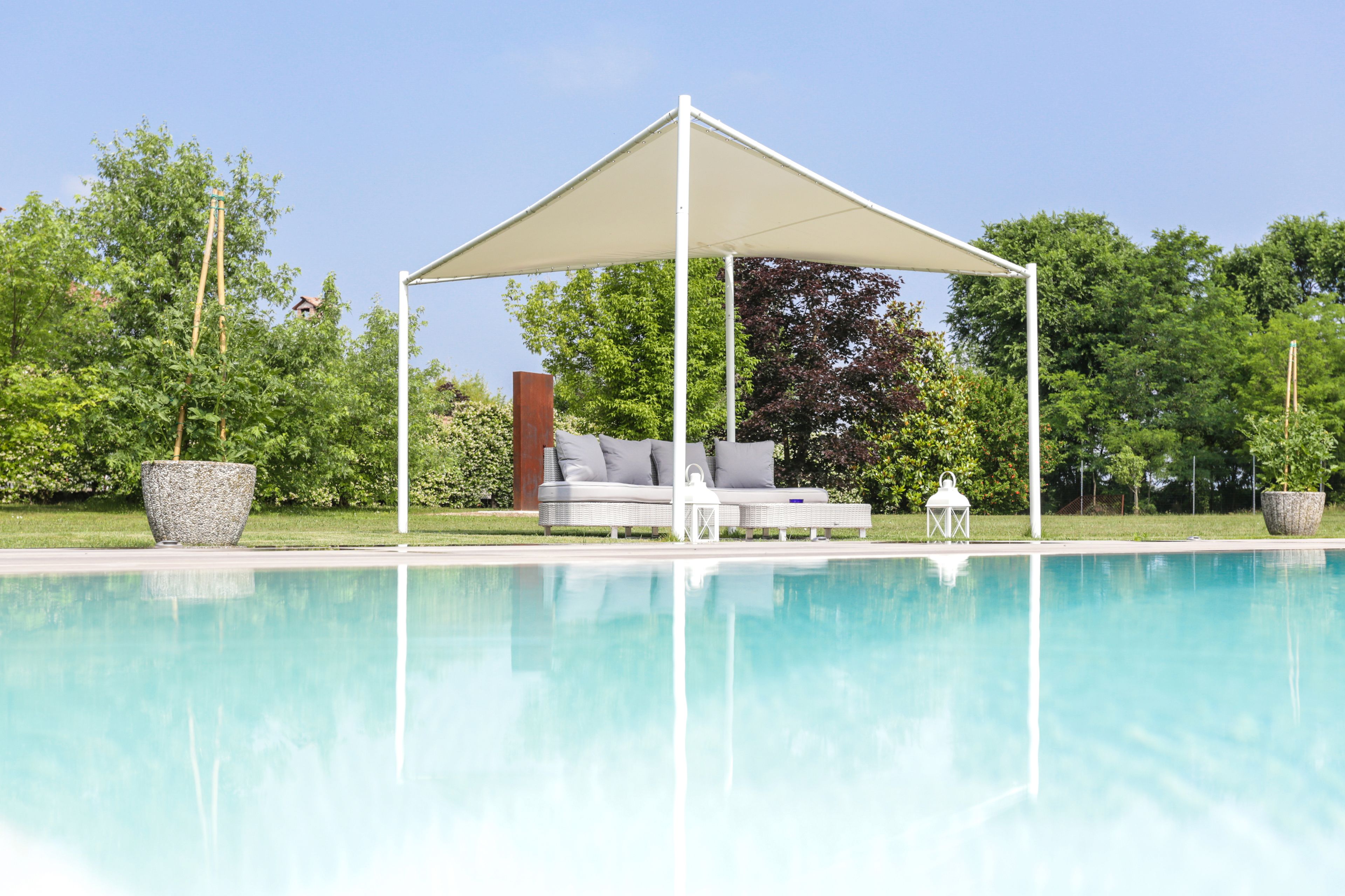 Area piscina con zona relax coperta, un divano da esterno bianco e una lanterna.