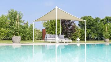 Area piscina con zona relax coperta, un divano da esterno bianco e una lanterna.