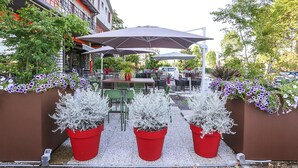 Een terras met tafels en stoelen, omringd door potplanten en bloemen.