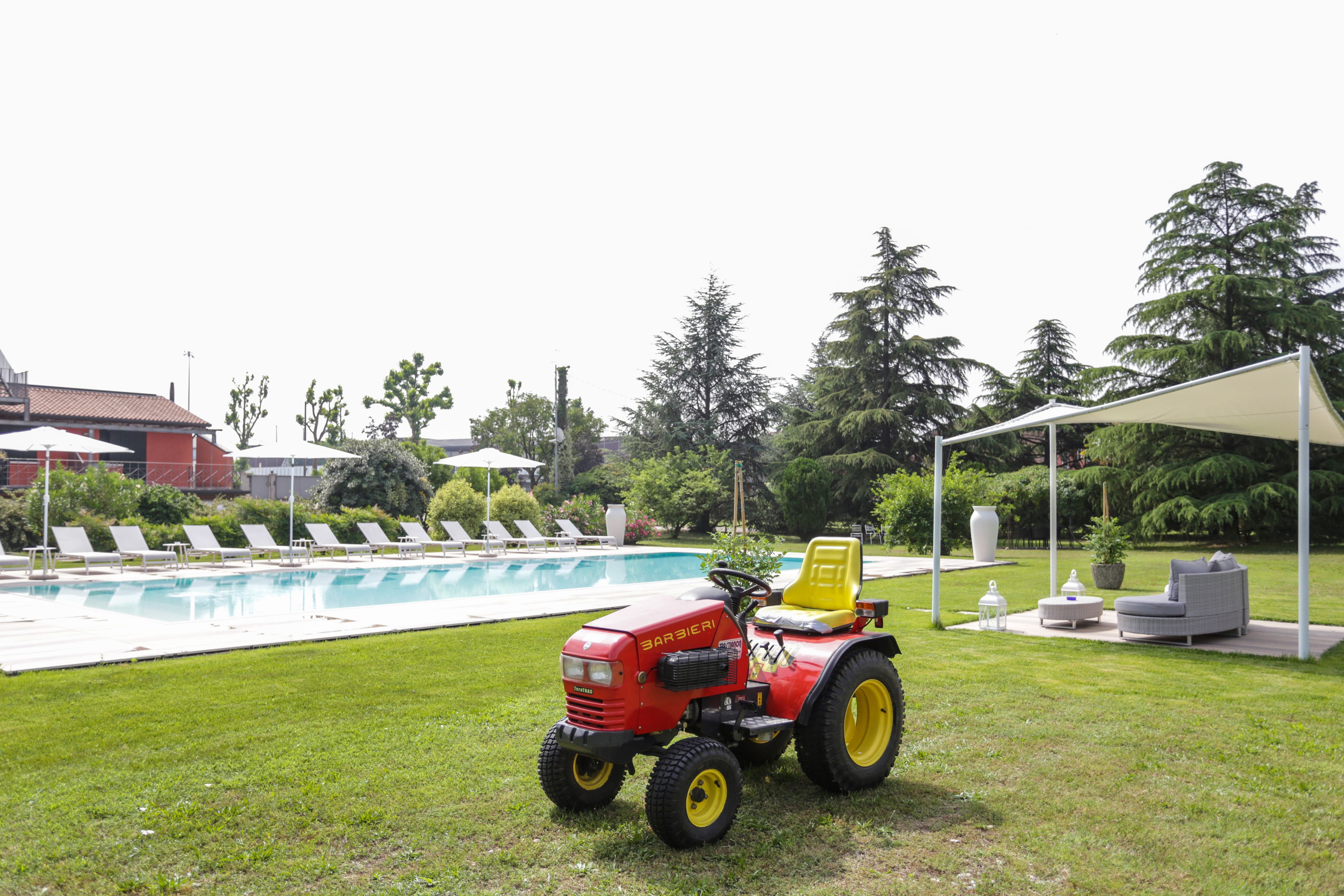 Un tractor rojo con asiento amarillo cerca de una piscina, rodeado de sillas de descanso y una zona de estar cubierta.