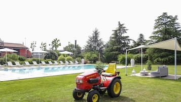 Un tractor rojo con asiento amarillo cerca de una piscina, rodeado de sillas de descanso y una zona de estar cubierta.