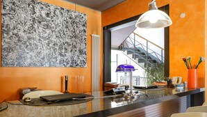 Een moderne hotellobby met een groot abstract schilderij, een receptiebalie, een trap en een potplant.