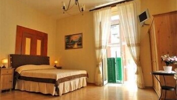 A bedroom with a bed, bedside tables, a painting, a television, and a view of the outside. - Domus Gemi (Naples)