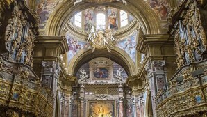 An ornate interior with high vaulted ceilings, intricate gold detailing, and a central altar. - Domus Gemi (Naples)