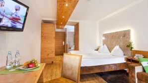 Una habitación de hotel moderna con una cama de madera, un televisor, una mesita con vasos y fruta, y techo de madera.