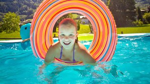 Una persona en una piscina con un círculo inflable de colores, rodeada por un cielo azul despejado y montañas distantes.