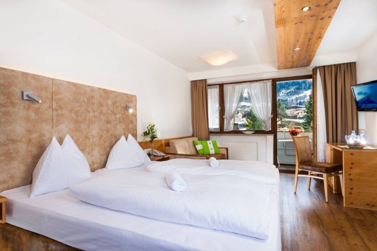 Hotelkamer met een groot bed, een bureau, een stoel, een televisie en een raam met uitzicht op de bergen.