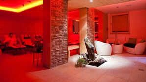 Un área de spa con suelos de madera, paredes de piedra e iluminación ambiental roja. Hay sillas de masaje y un mostrador de recepción.