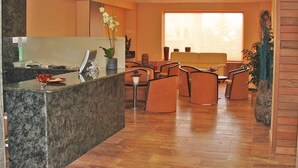 Un espace d’accueil doté d’un comptoir en marbre, de plusieurs chaises, d’un canapé et d’une grande fenêtre avec des stores.