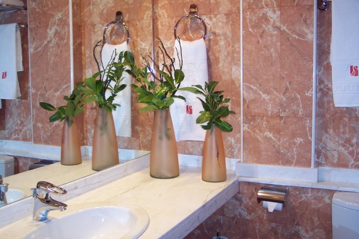 A bathroom with a marble wall, a sink, and three vases with plants.
