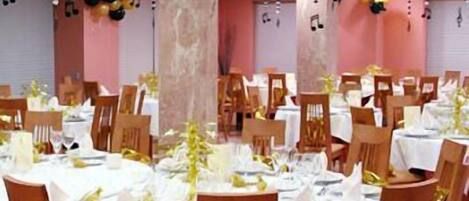 Un salón de banquetes con mesas redondas cubiertas con manteles blancos, sillas de madera y decoraciones colgantes.