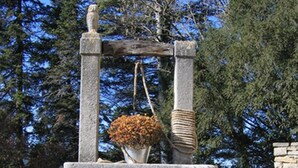 Une structure en pierre sur laquelle est suspendu un pot de fleurs et un seau.