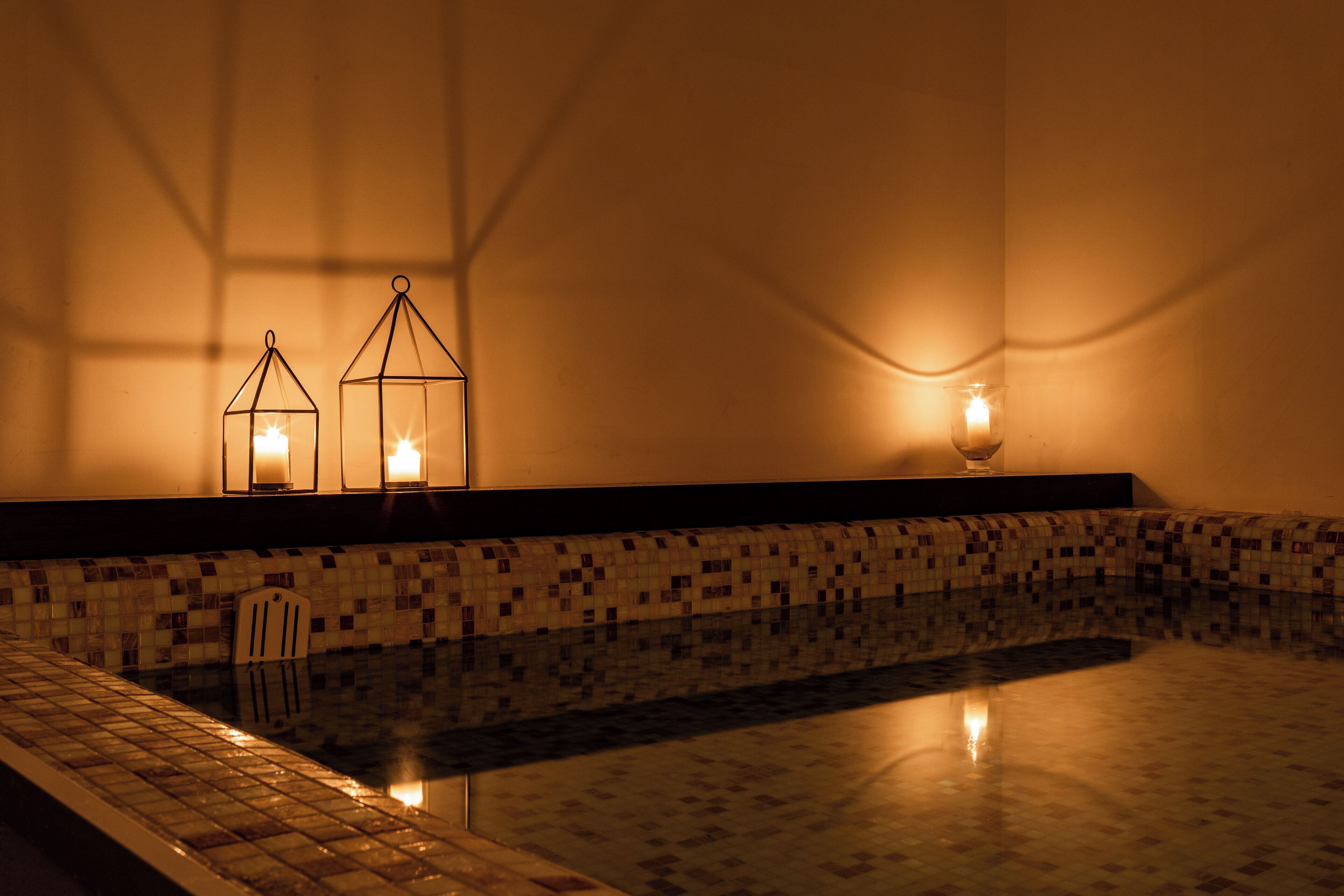 A pool area with tiled flooring and a low wall. There are two candle-like lights on the wall.