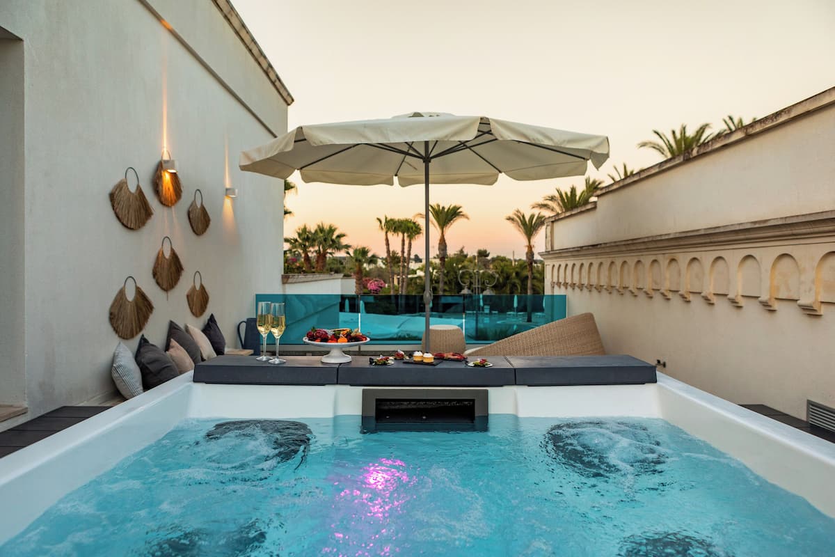 Un jacuzzi con una mesa lista para una comida, rodeado por una piscina y un área de descanso con una sombrilla.