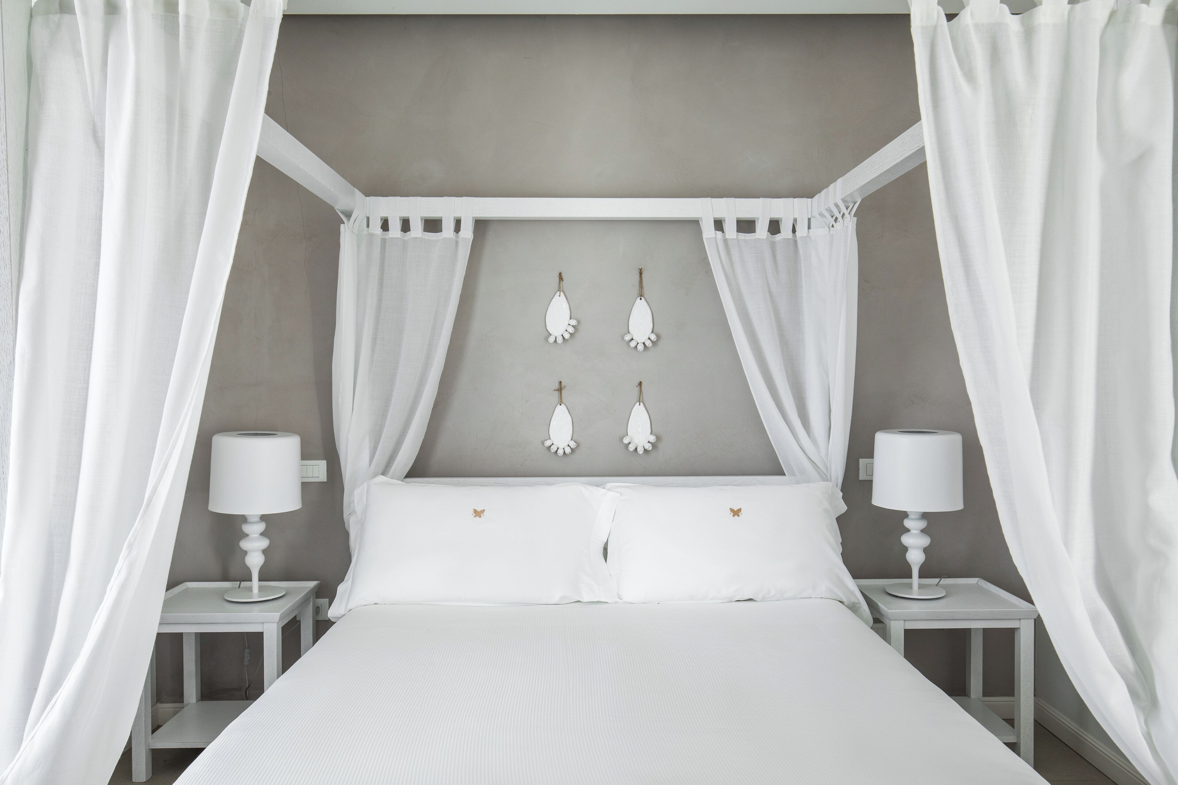 A bedroom with a canopy bed, two bedside tables with lamps, and decorative wall hangings.