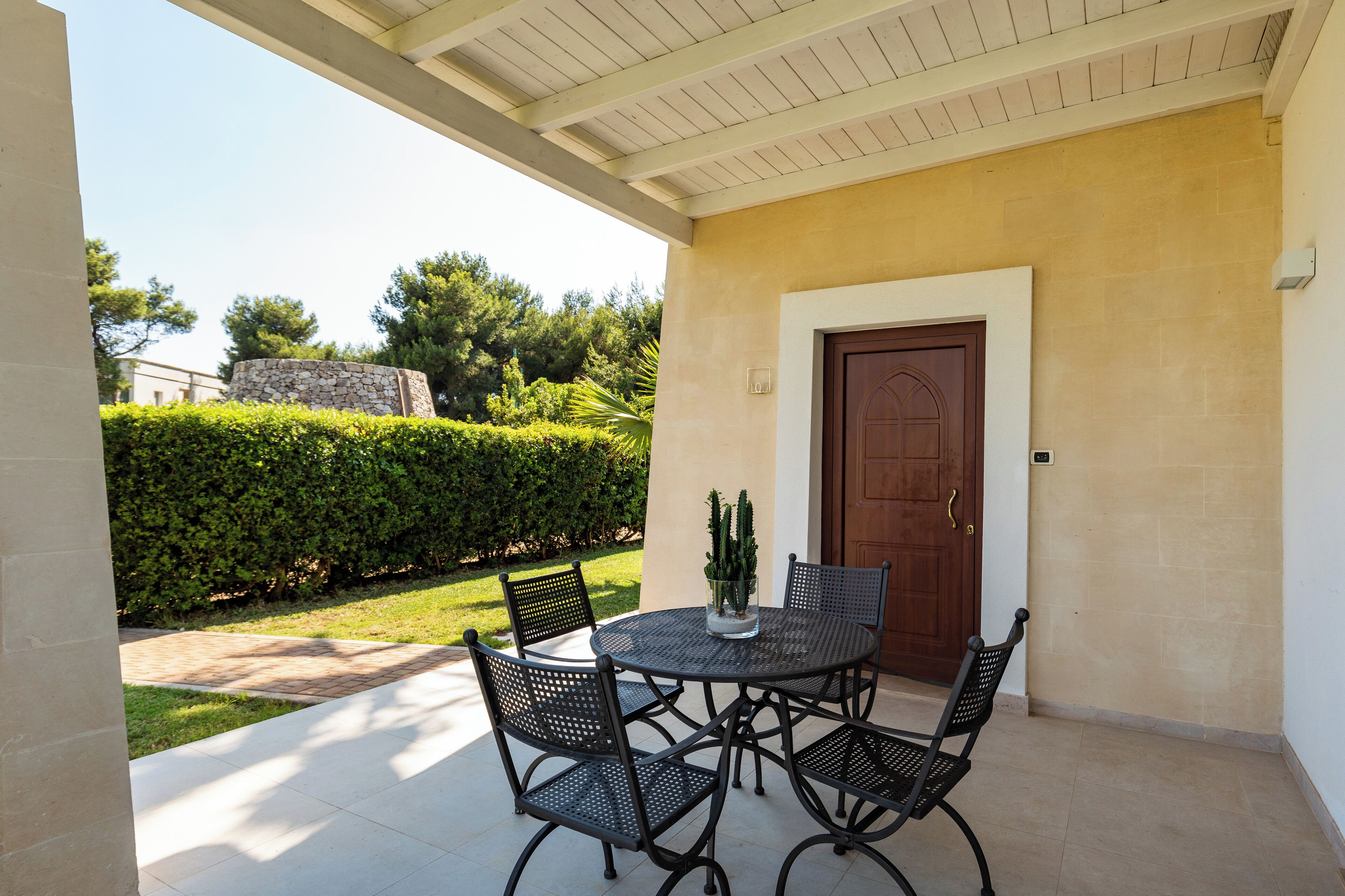 A patio with a round table and four chairs, a cactus centerpiece, and a wooden door.