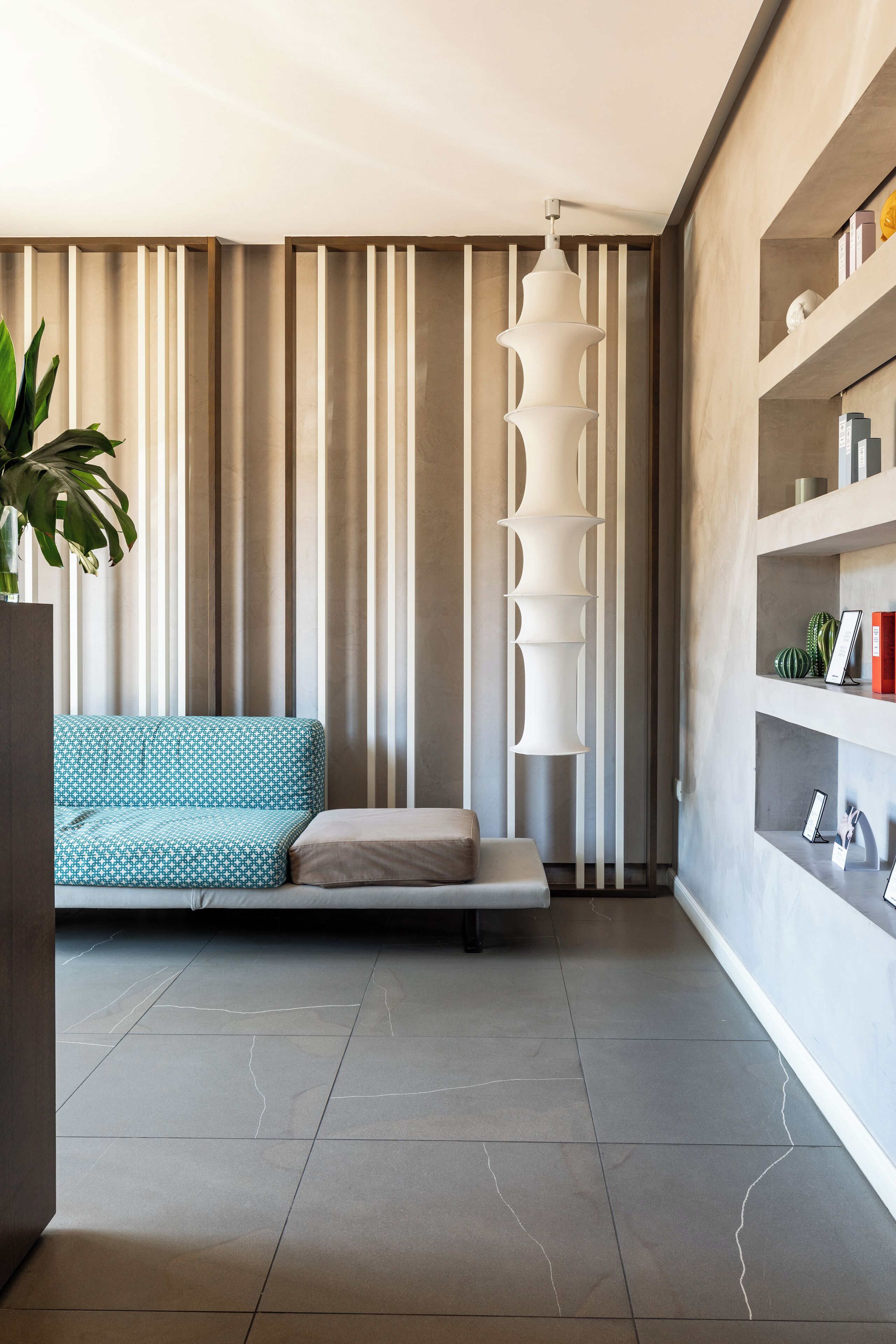 A modern living room with a sofa, a tall white light fixture, and a plant.