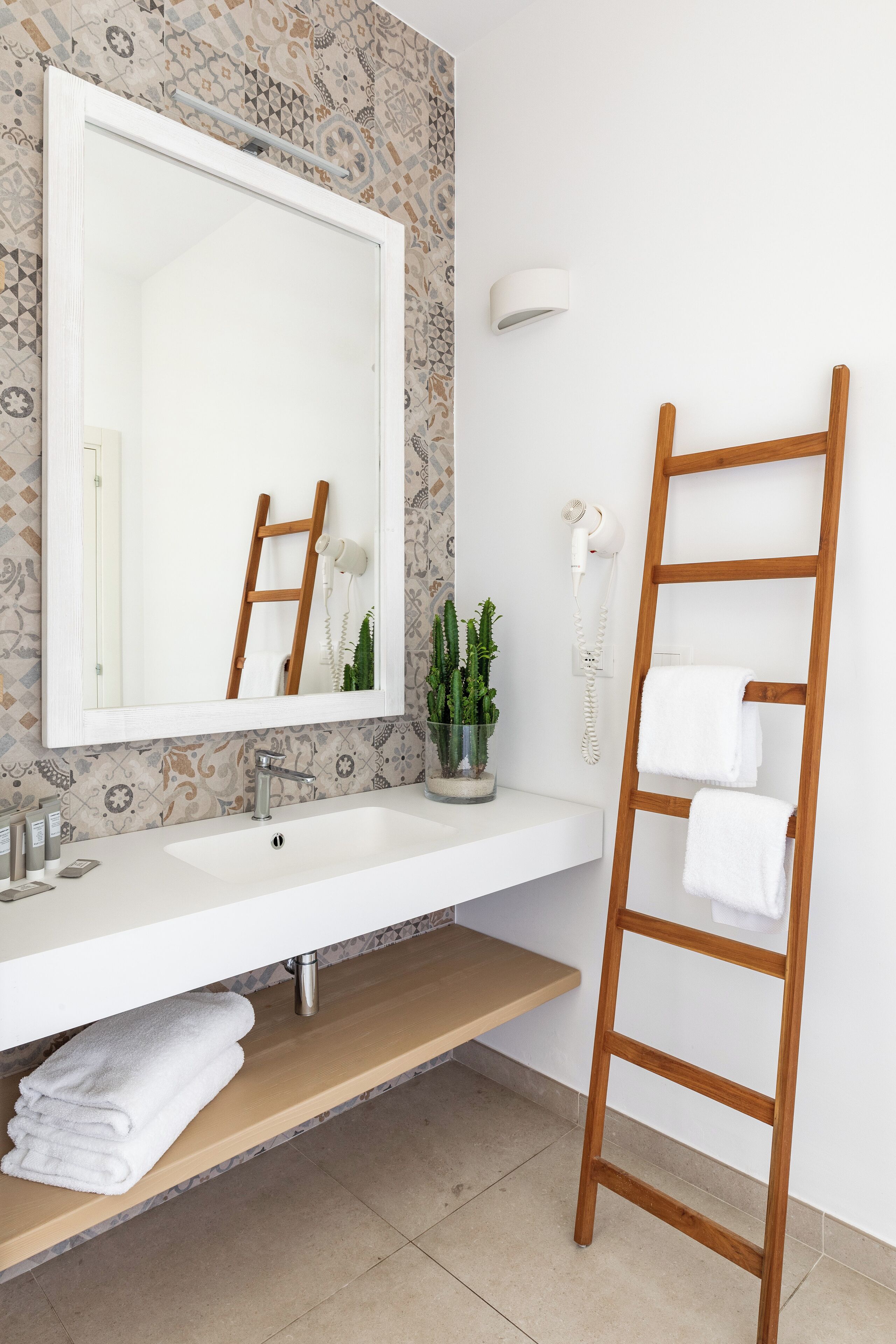 A bathroom with a large mirror, white sink, wooden ladder, and a potted plant.